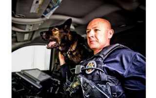 Dog leaning over a man's shoulder in a police car