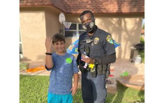 Police officer standing next to young male who is smiling and holding up his right arm to show bracelet that officer gave to him