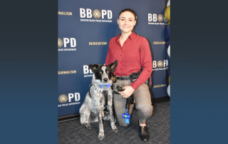 Police woman kneeling next to a white and black dog